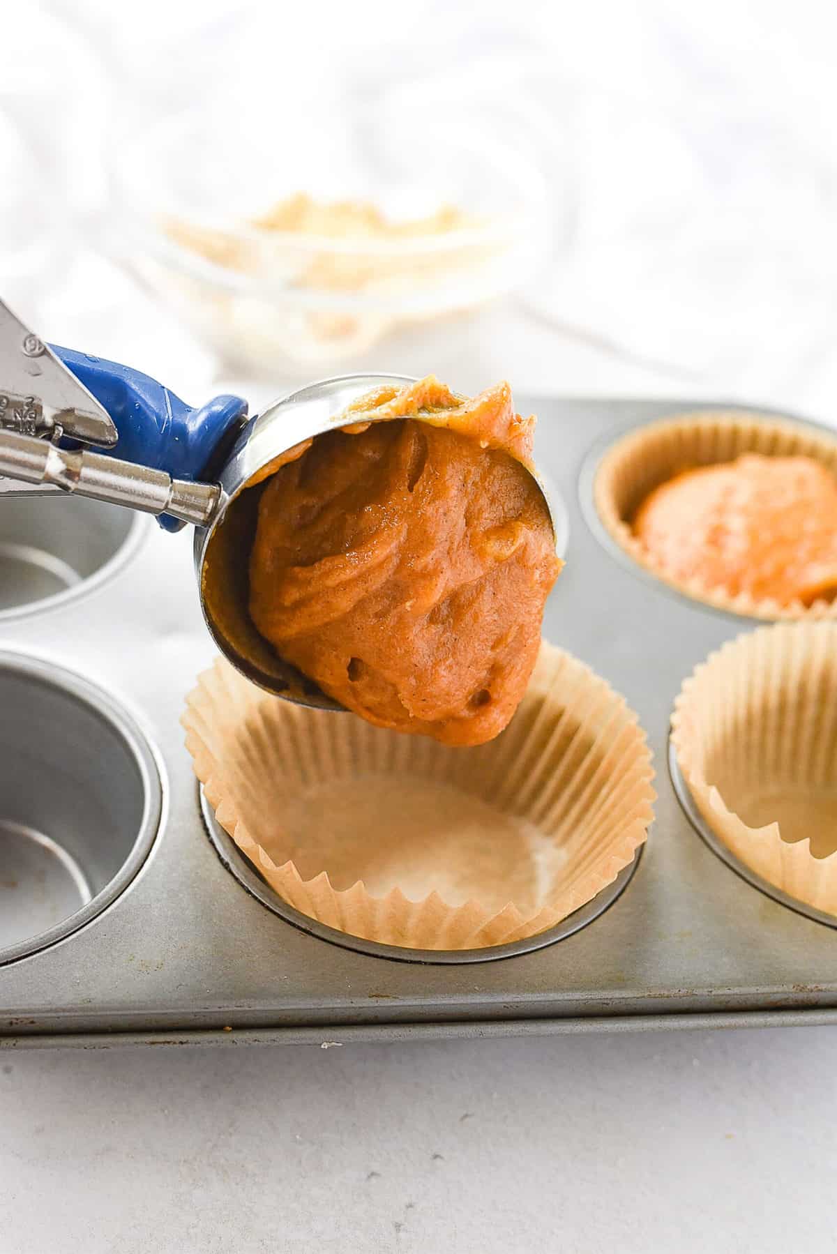 scooping pumpkin muffin batter into muffin tin