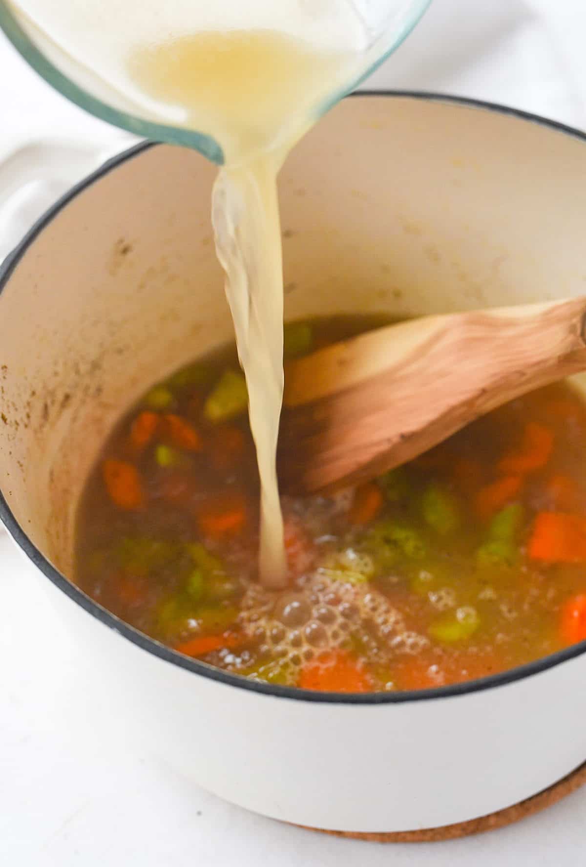 pouring chicken broth into pan