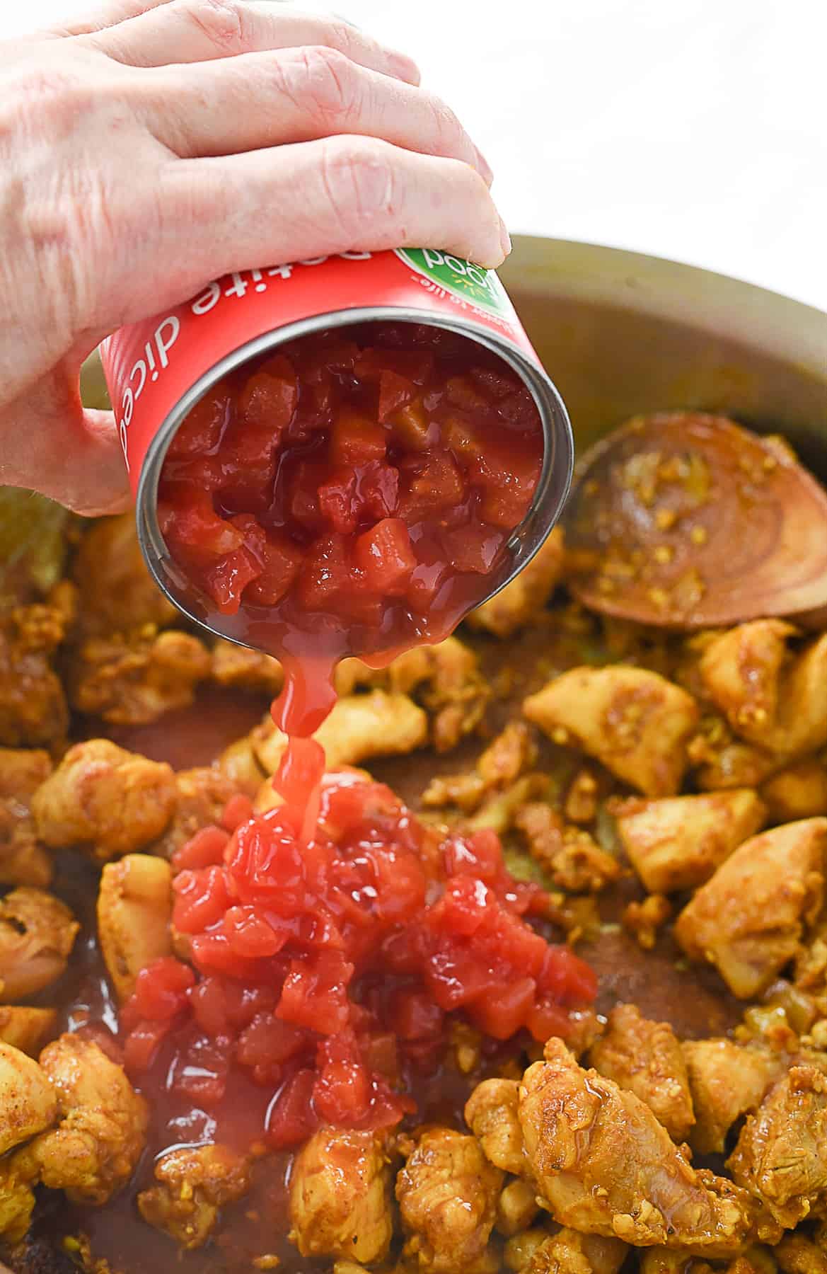 pouring tomatoes into chicken curry