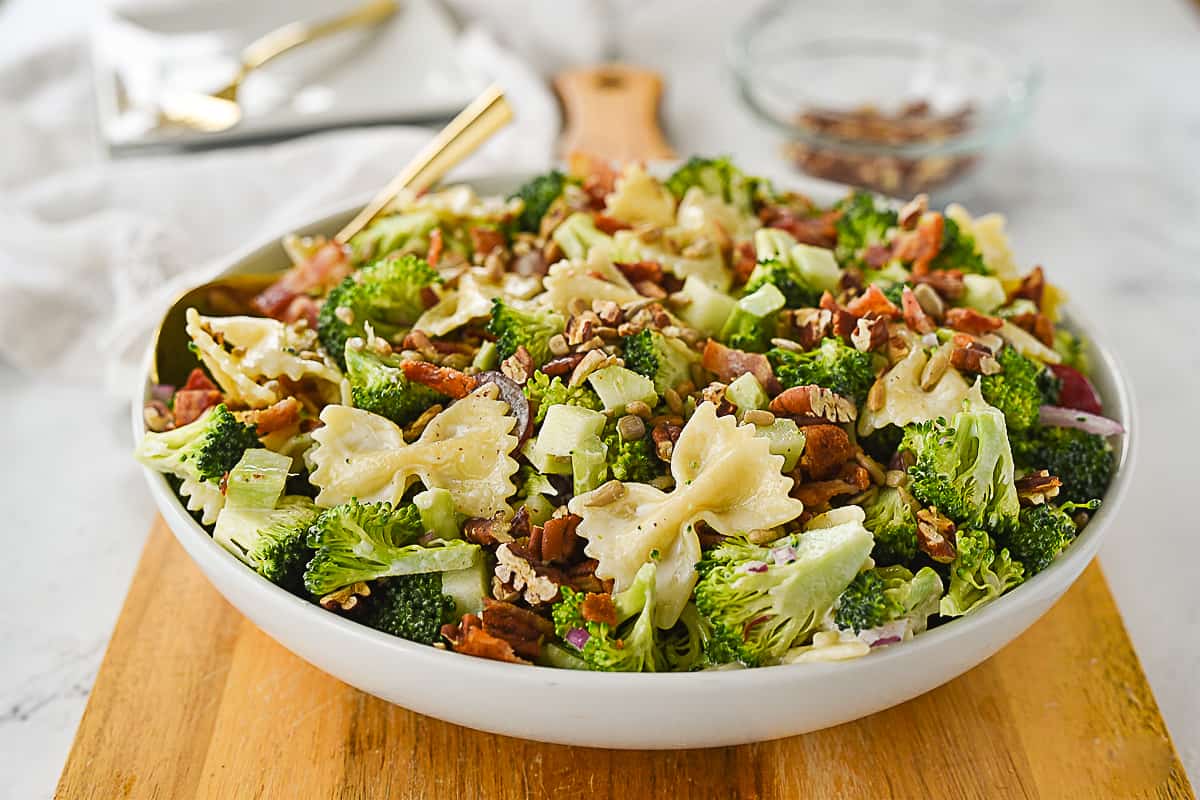 broccoli pasta salad in white bowl sitting on a cutting board