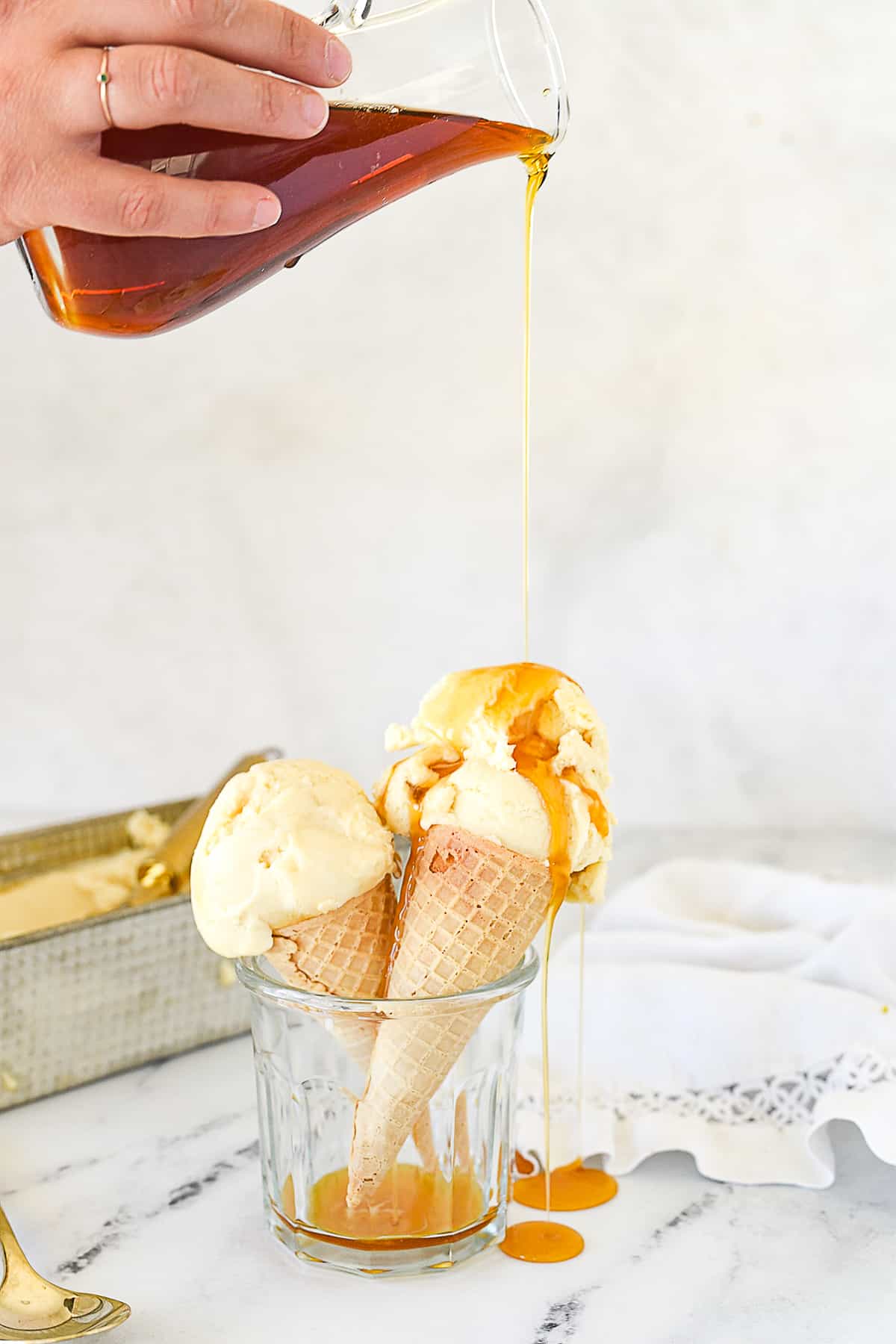 hand pouring maple syrup over an ice cream cone