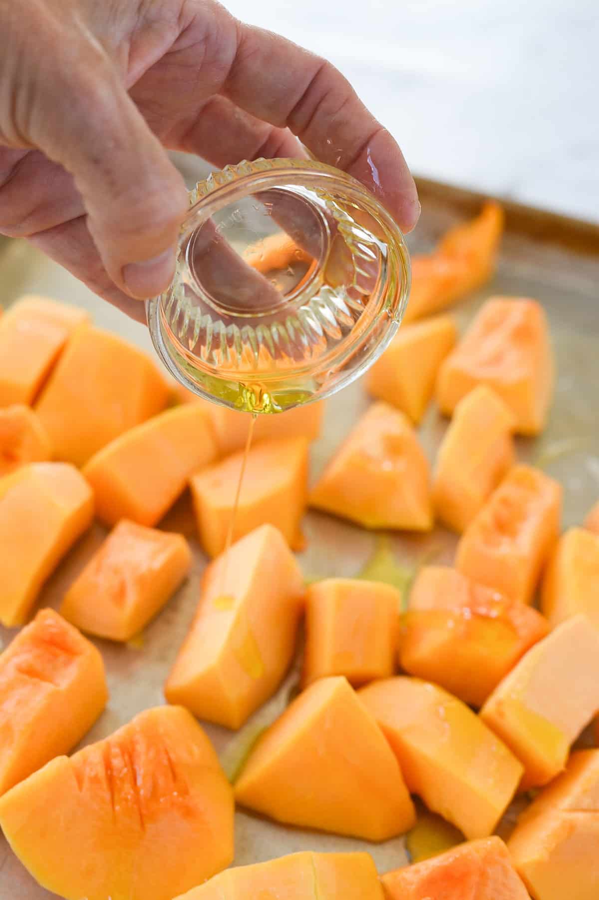 pouring olive oil over butternut squash
