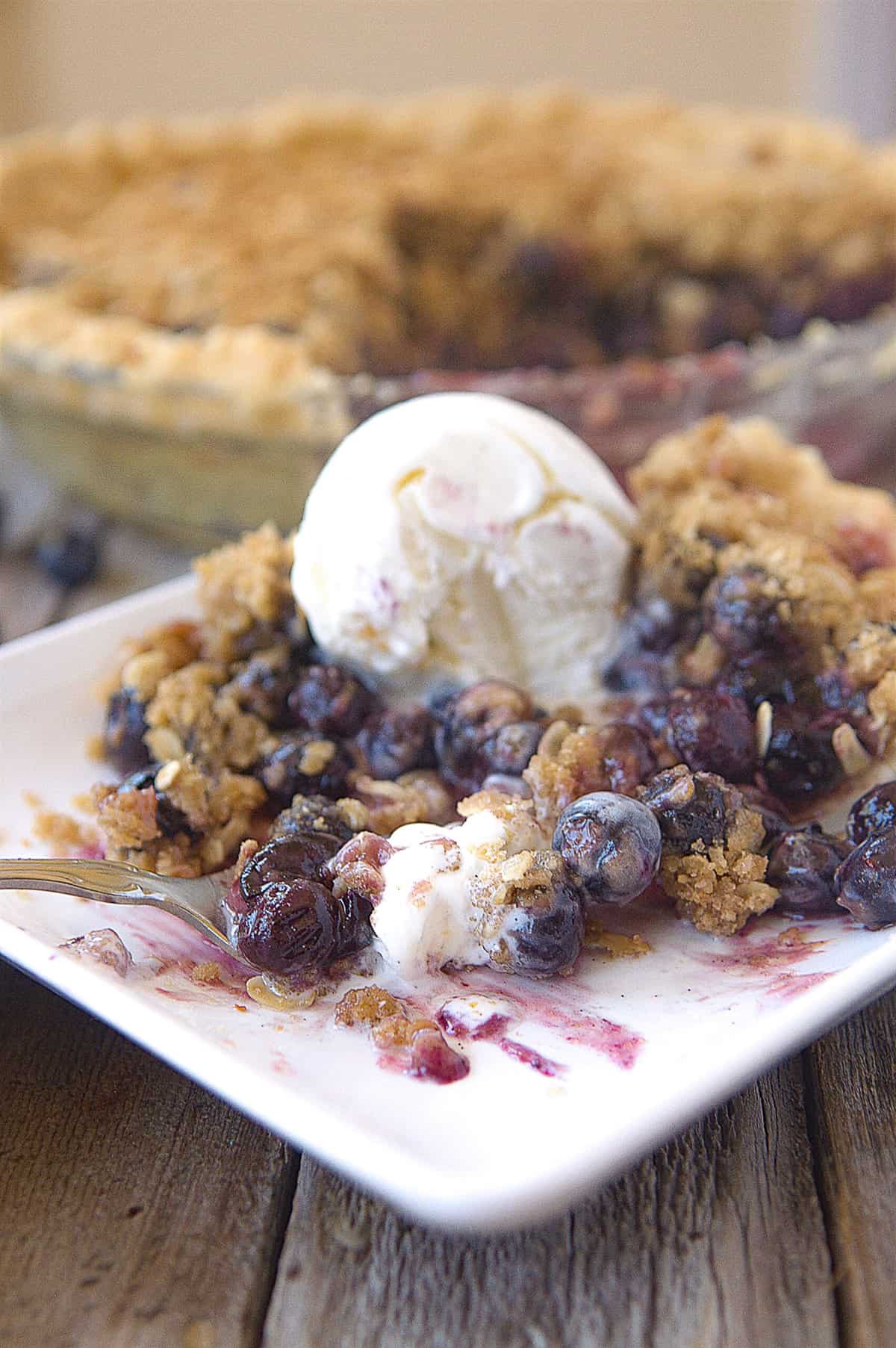 Blueberry Pie fork on a plate of blueberry pie with ice cream on top