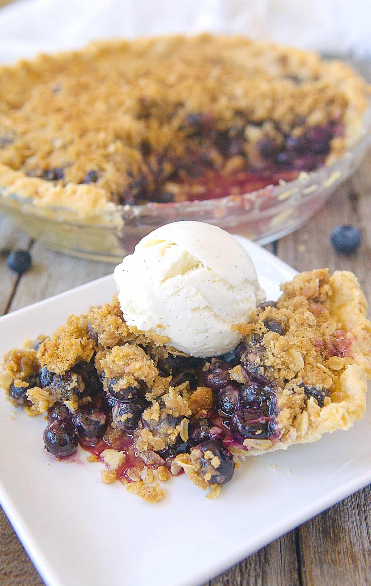 slice of blueberry pie with ice cream on a white plate