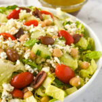 white bowl with greek salad and a bowl of dressing