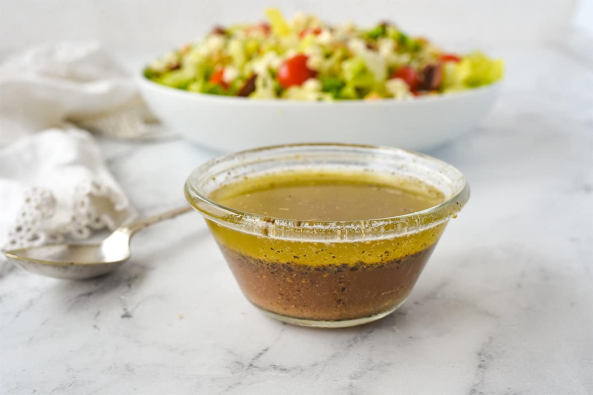 greek salad dressing in a bowl in front of a salad