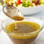 spoon drizzling greek salad dressing in a bowl