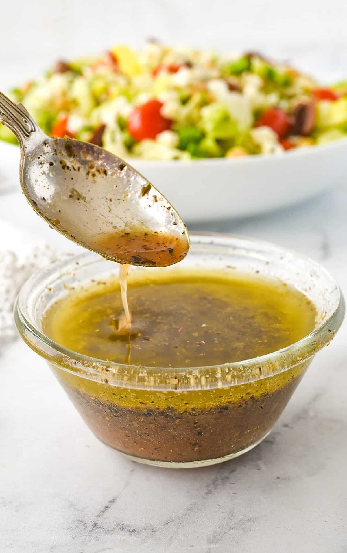 spoon drizzling greek salad dressing in a bowl
