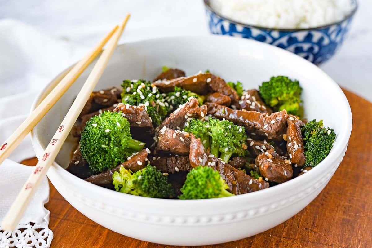 beef and broccoli in a white bowl topped with sesame seeds