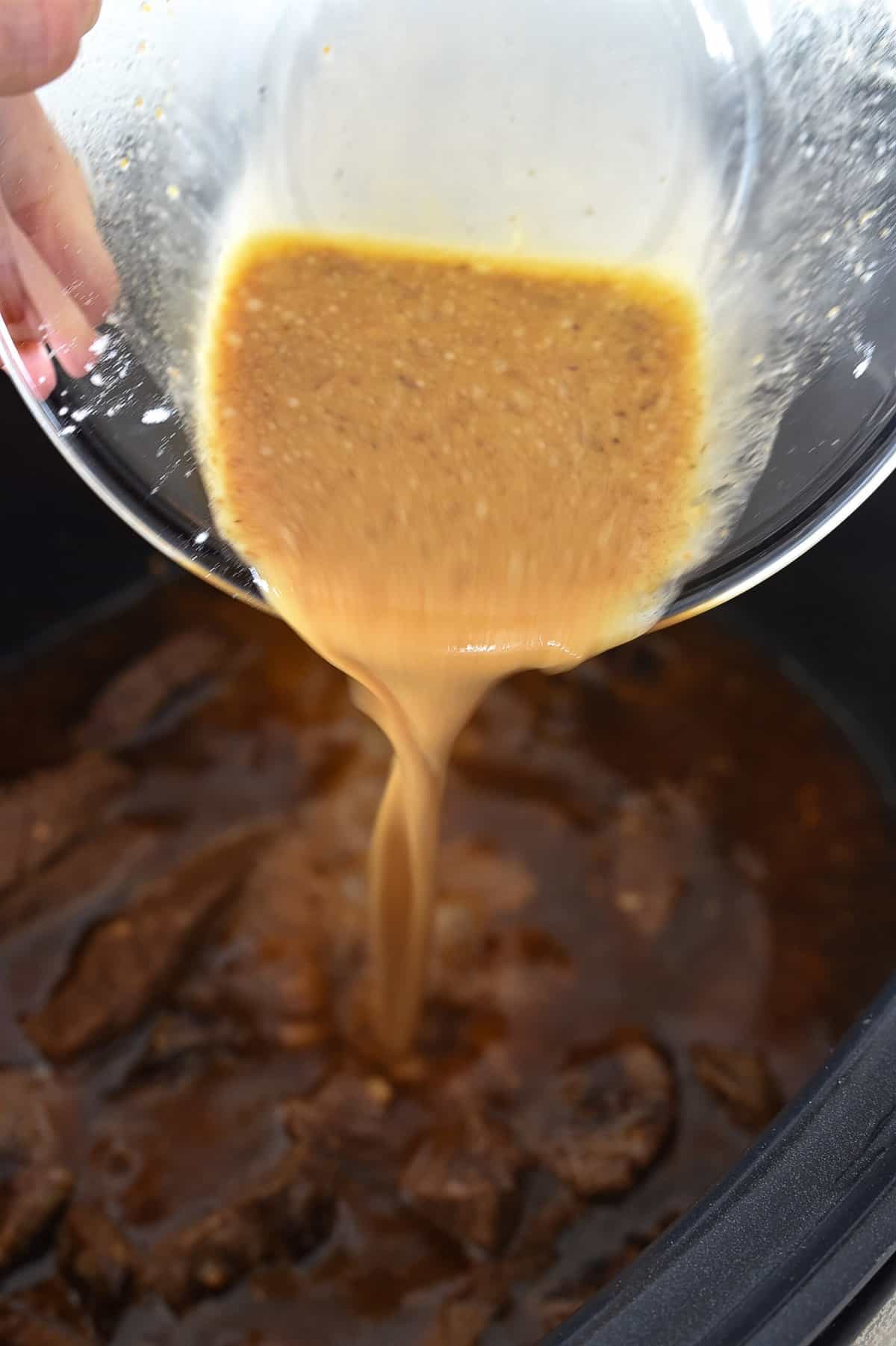 pouring liquid over meat in crock pot
