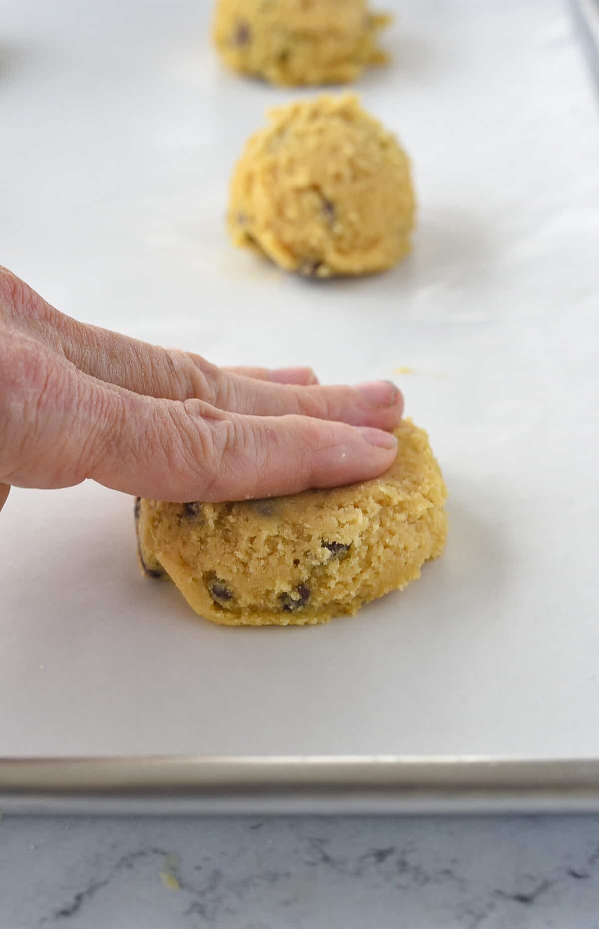 hand flattening cookie dough on baking sheet
