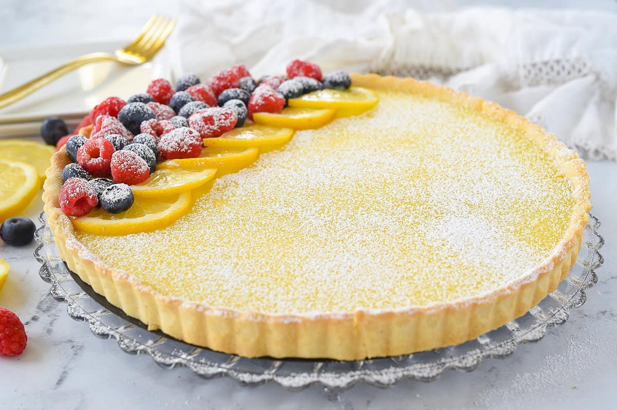 lemon curd fruit tart on a serving plate with raspberries and blueberries on top