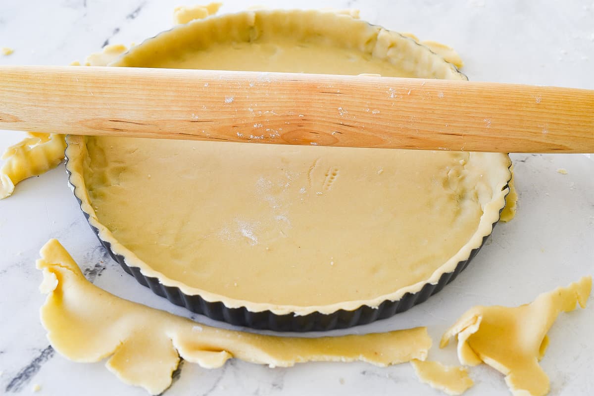 Rolling pin over top of tart pan to trum off dough