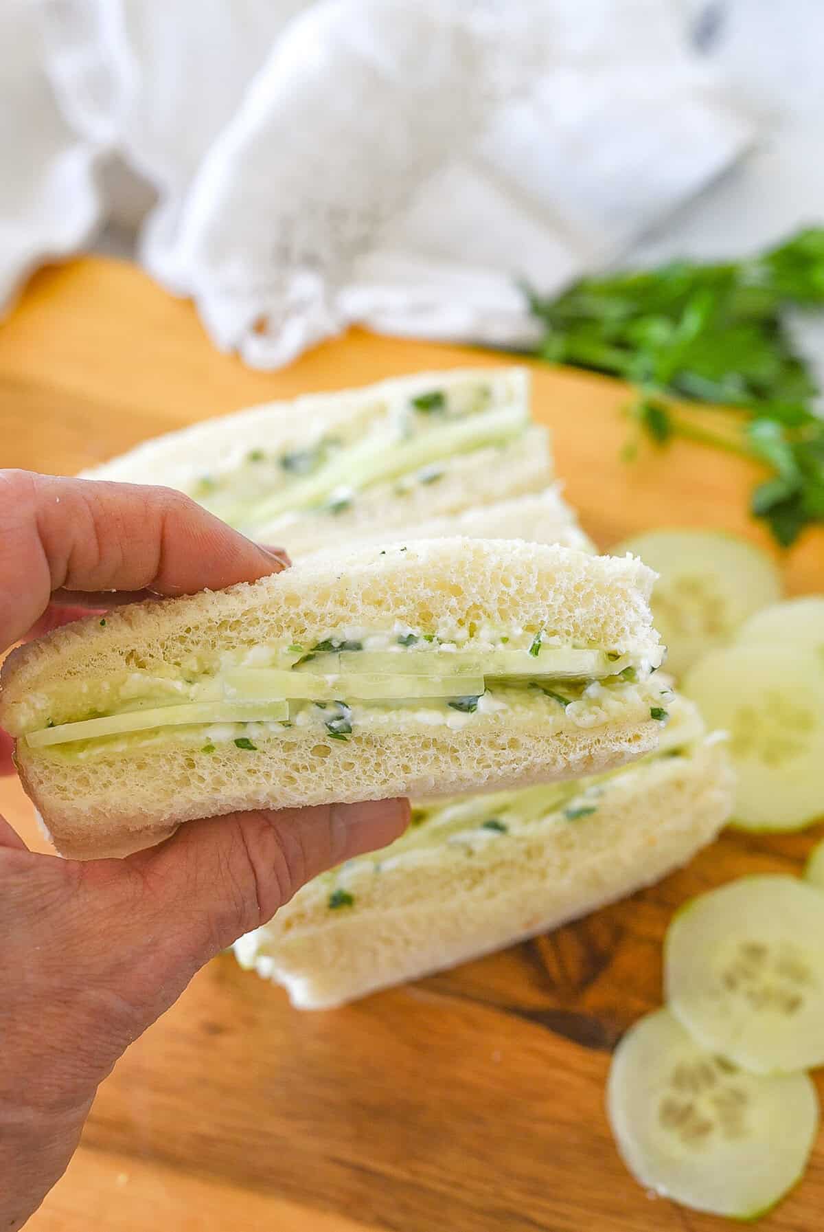 hand holding a cucumber sandwich