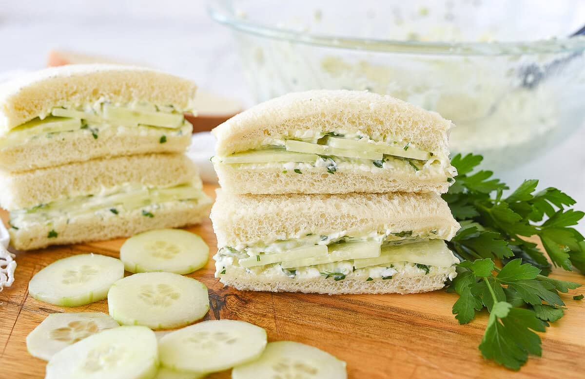 four cucumber sandwiches on a cutting board with sliceds of cucumber