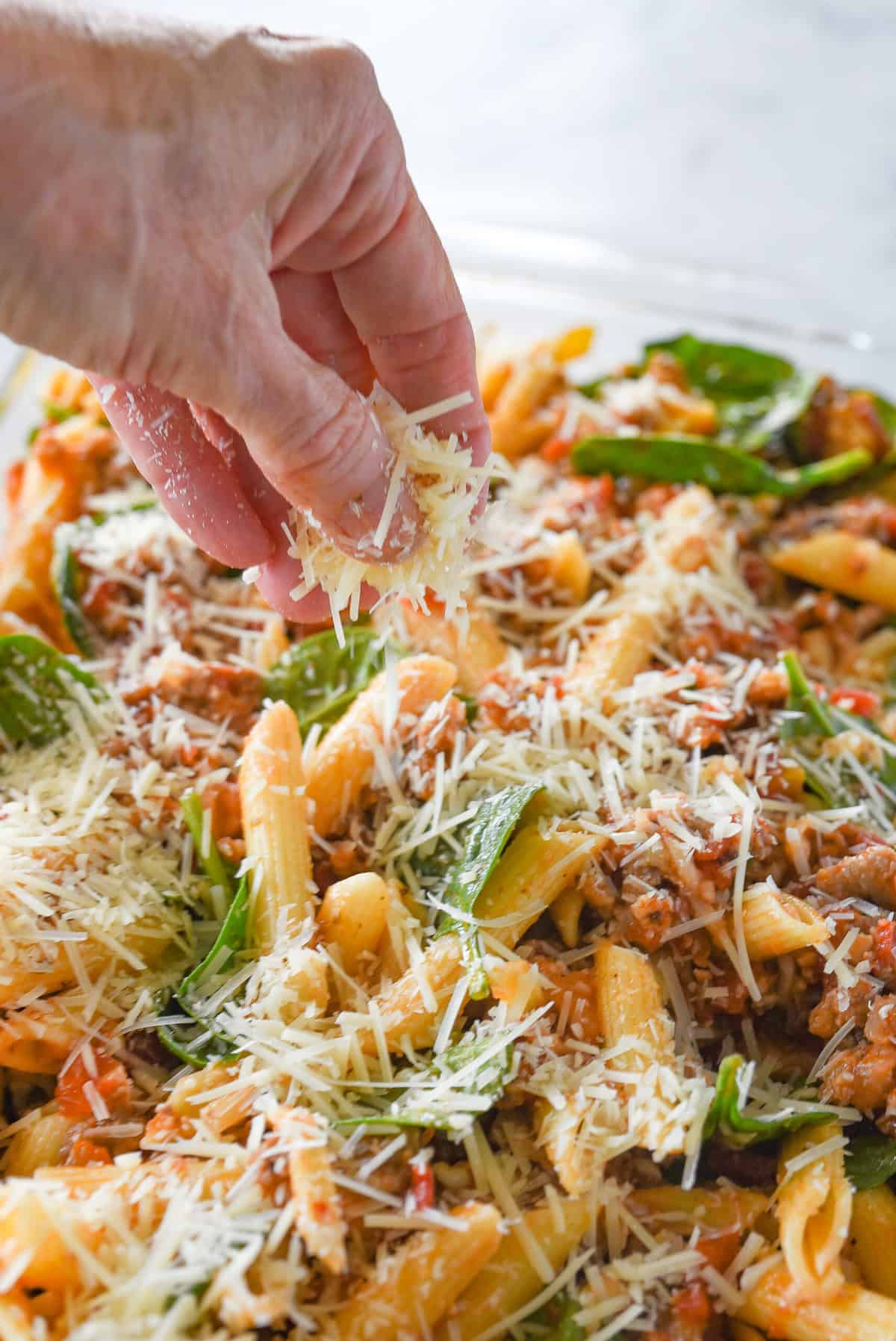 sprinkling cheese on top of ziti