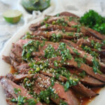sliced flank steak on a white plate with c himchurri on top