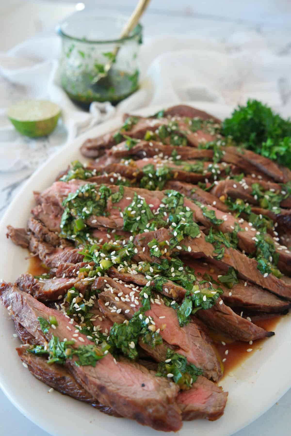 sliced flank steak on a white plate with c himchurri on top