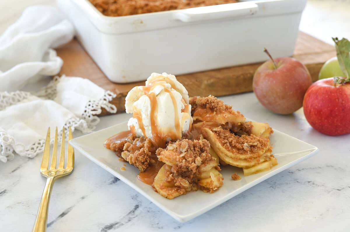 apple crisp on a whtie plate with ice cream on top