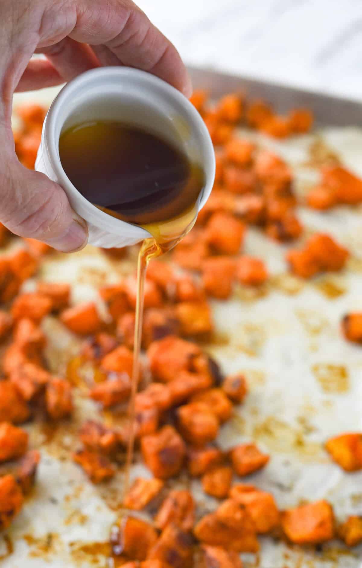 pouring maple syrup over roasted sweet potatoes