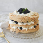 brown sugar pavlova with whipped cream and berries on top on a clear glass plate