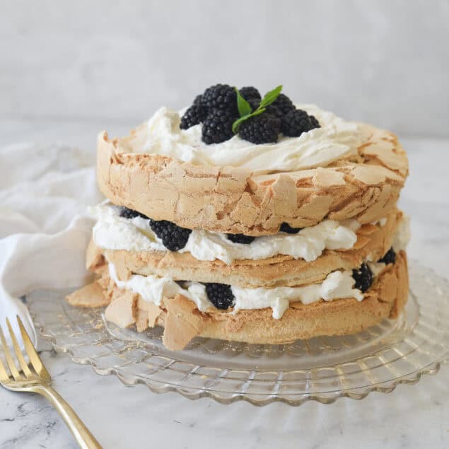 brown sugar pavlova with whipped cream and berries on top on a clear glass plate
