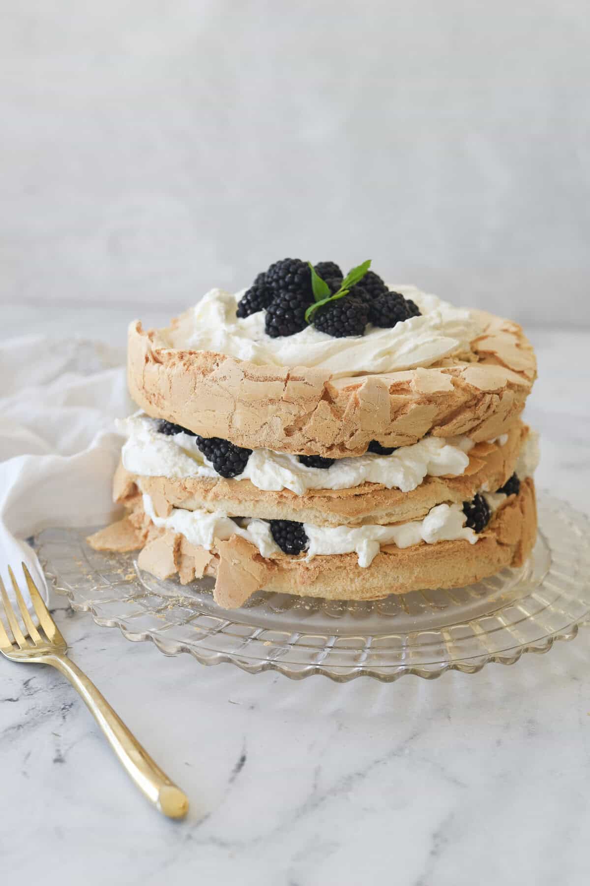 brown sugar pavlova with whipped cream and berries on top on a clear glass plate