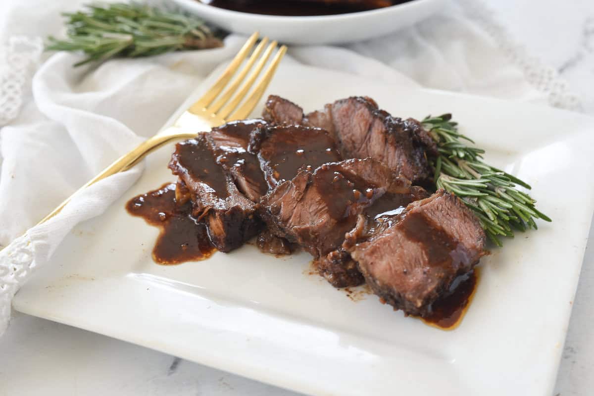 sliced short rib on white plate with rosemary garnish'
