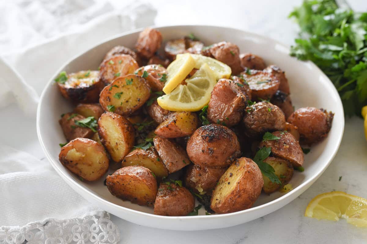 greek lemon potatoes in a white bowl with slices of lemon on top