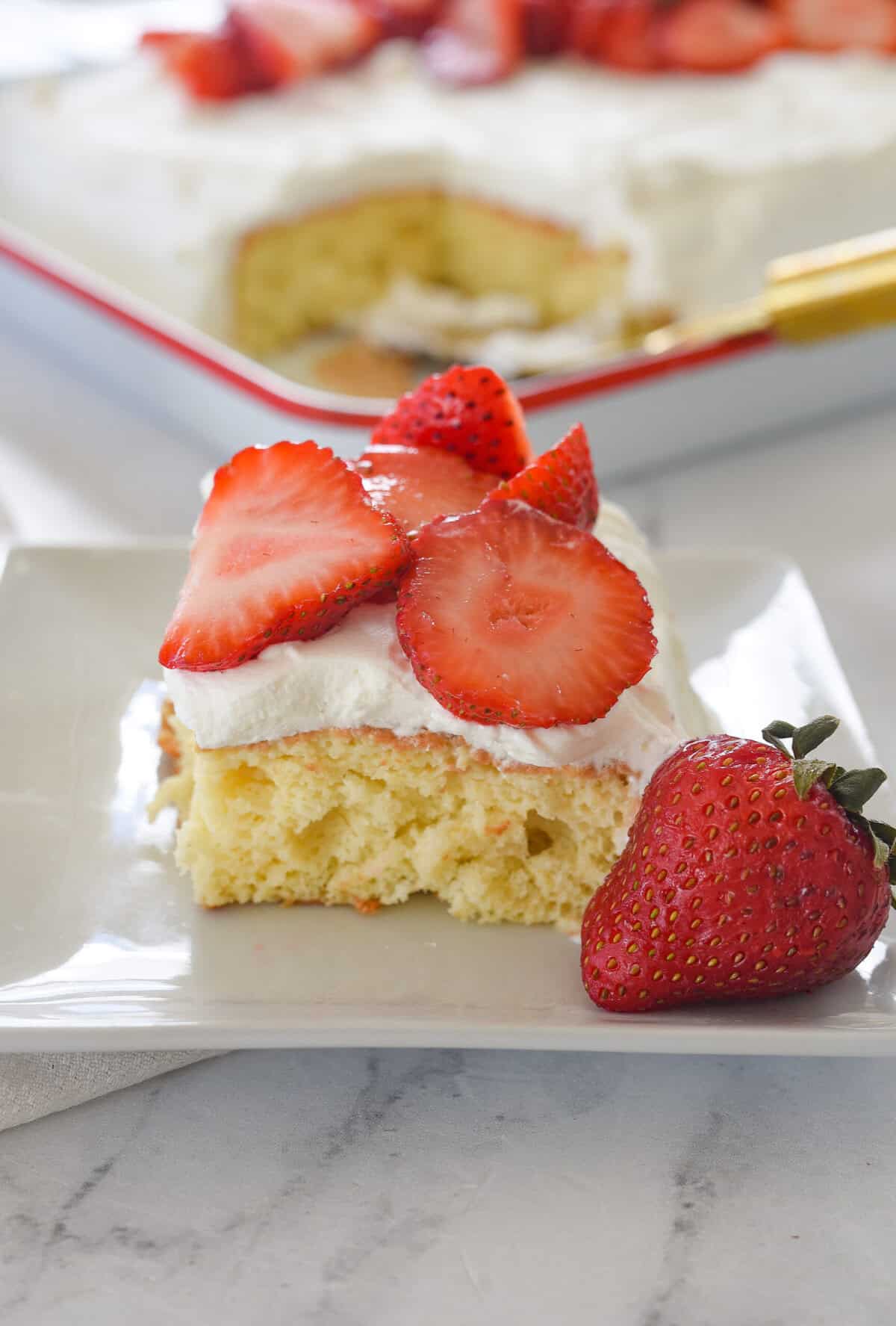 slice of tres leches cake on a plate with strawberries on top