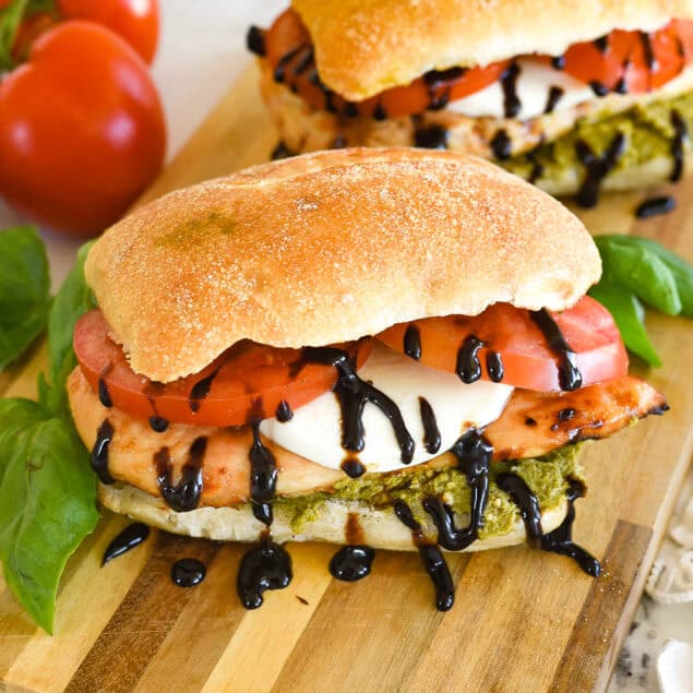 two chicken caprese sandwiches on a cutting board