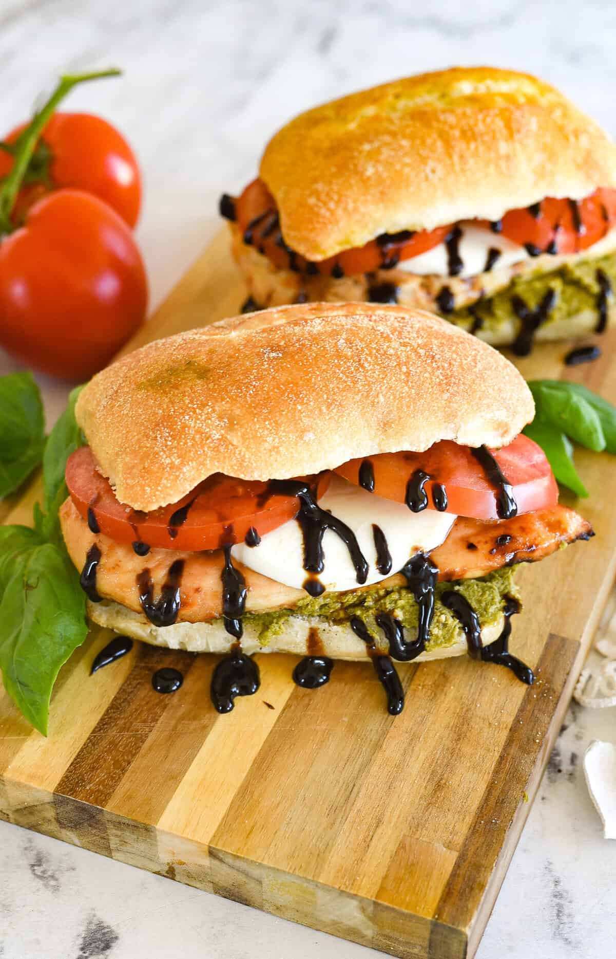 two chicken caprese sandwiches on a cutting board