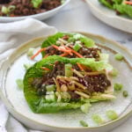 plate with two beef lettuce wraps on it and a bowl of korean beef