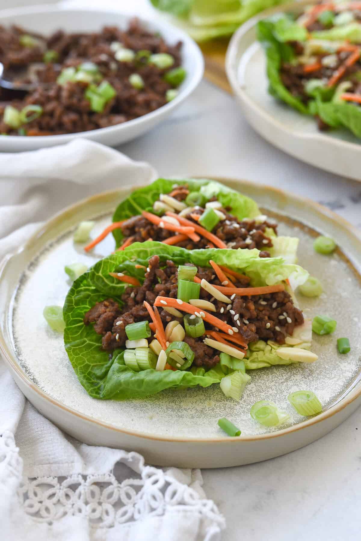 plate with two beef lettuce wraps on it and a bowl of korean beef