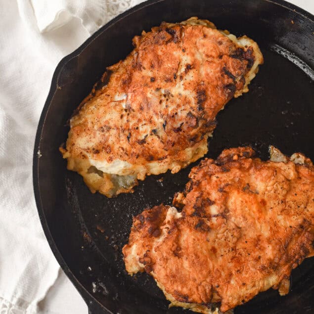 two buttermilk chicken breasts in a cast iron pan