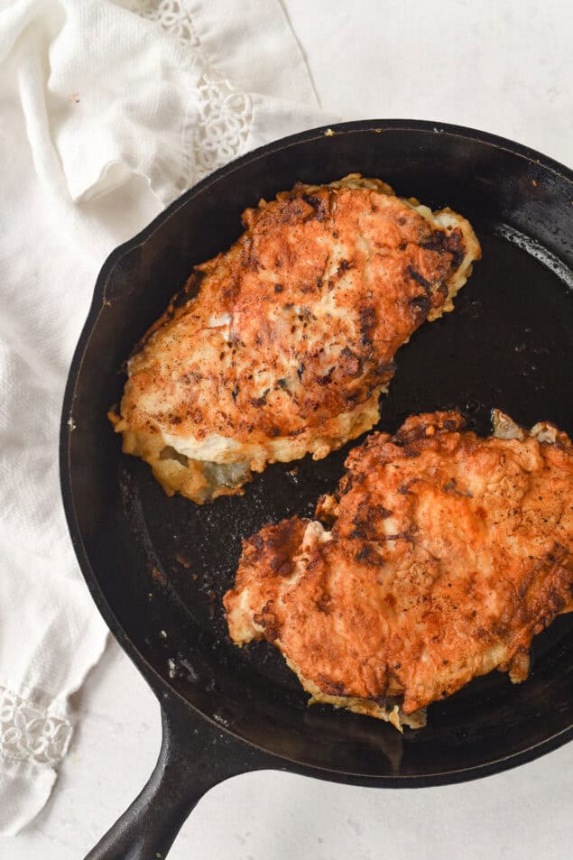 two buttermilk chicken breasts in a cast iron pan