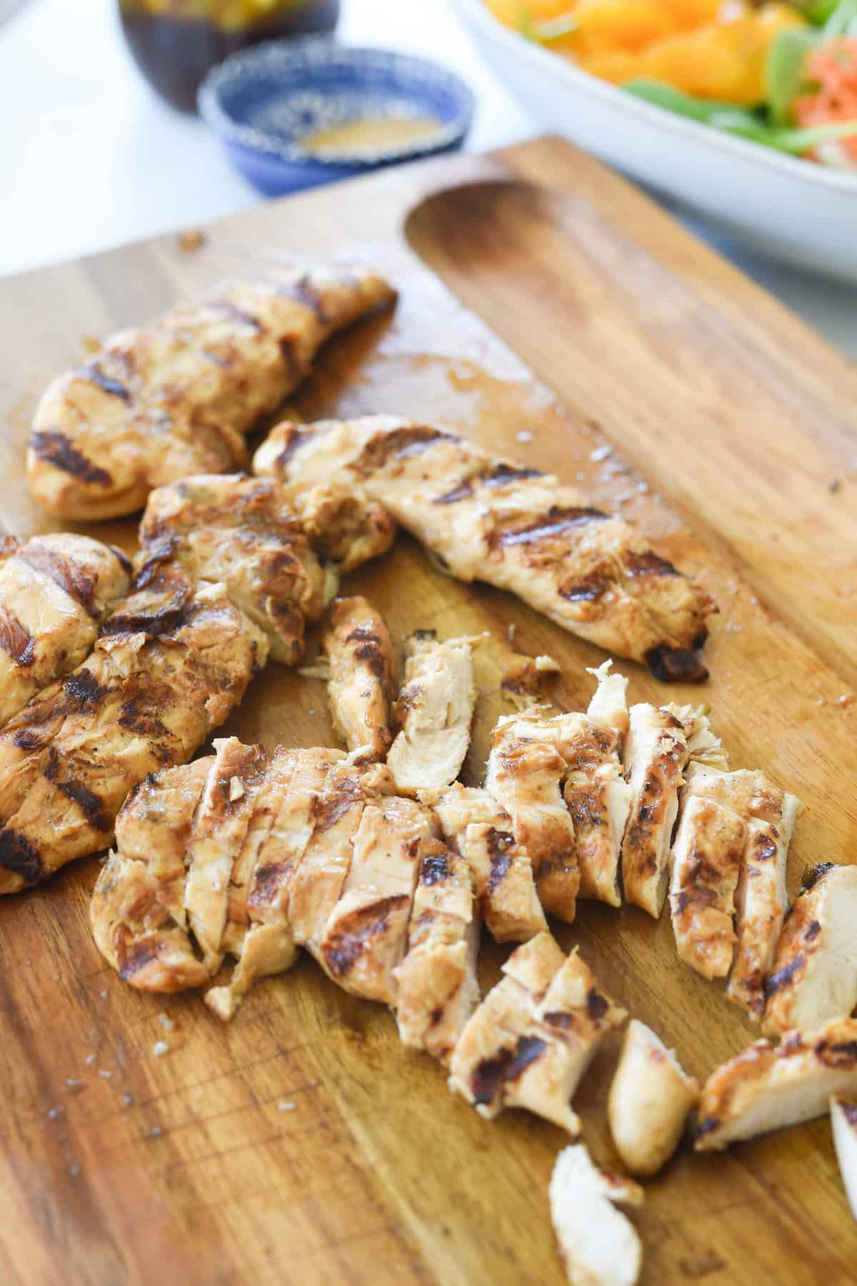 grilled chicken being cut into pieces on cutting board