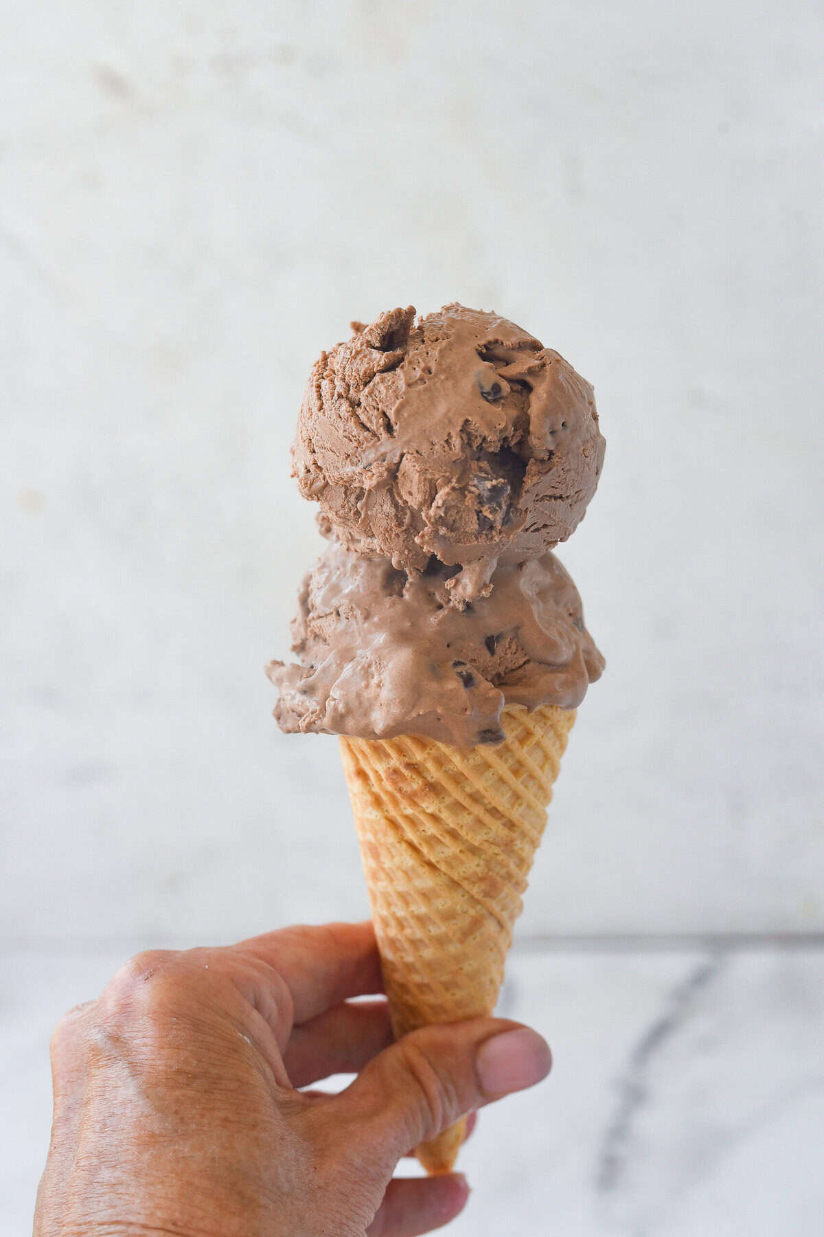 chocolate ice cream cone with hand holding it