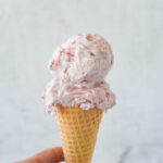 strawberry ice cream cone in a hand.