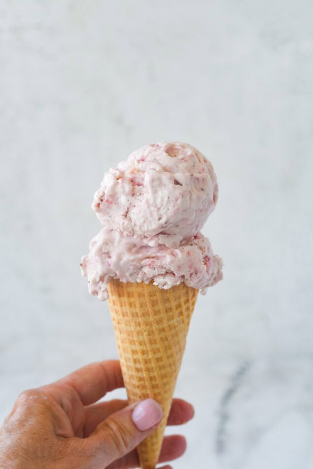 strawberry ice cream cone in a hand.