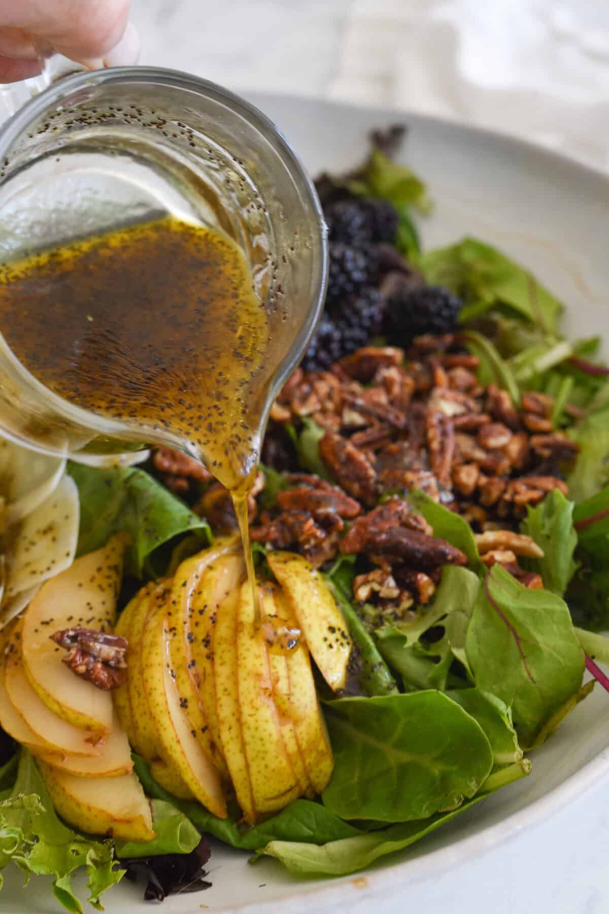 pouring poppy seed dressing over a salad