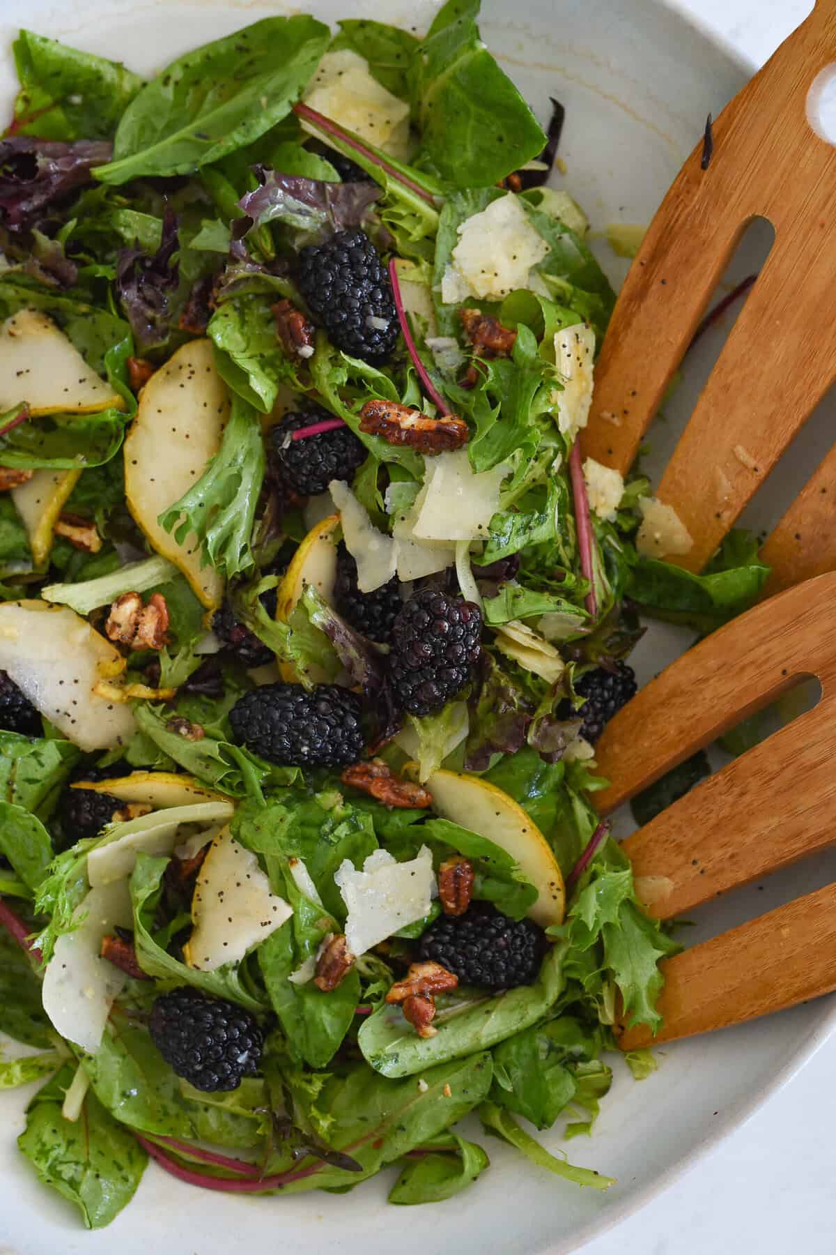tossing blackberry and pear salad in a white bowl
