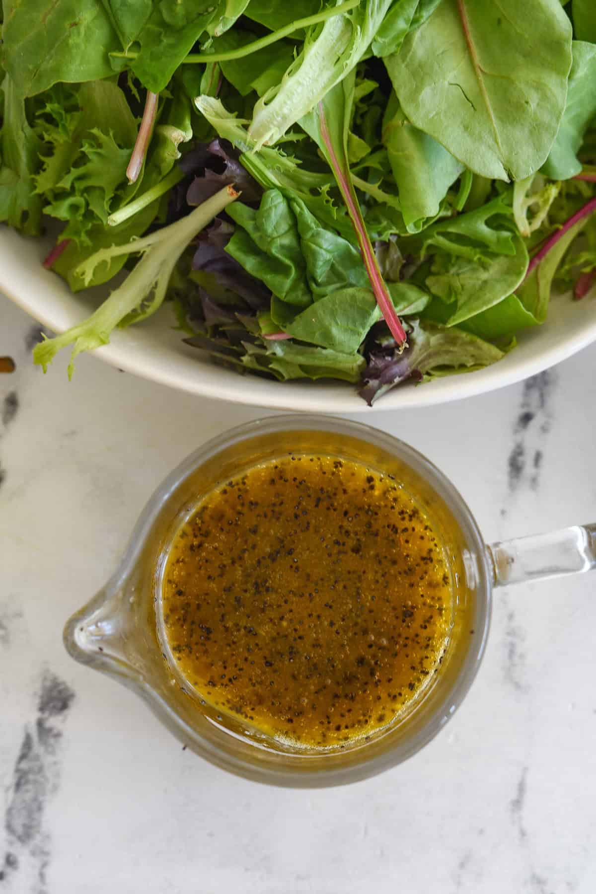 overhead shot of salad poppy seed dressing in a pitcher with a bowl of lettuce