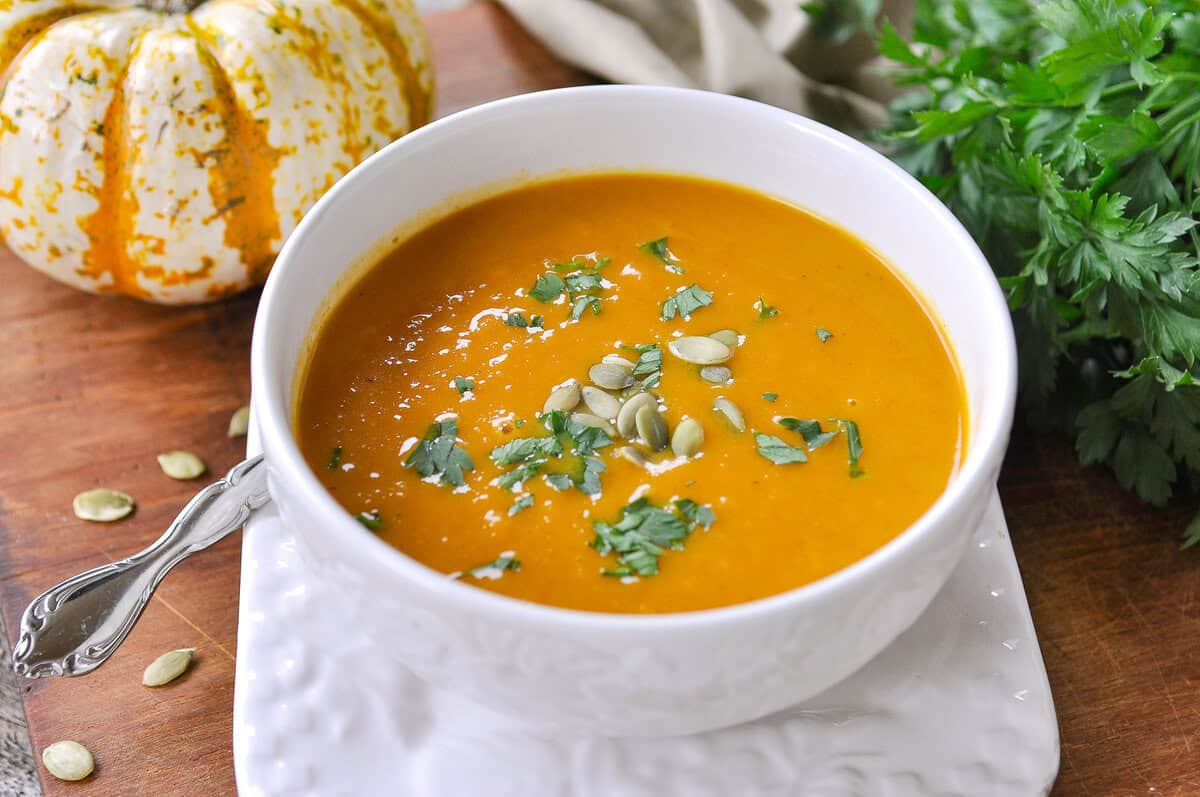 white bowl on a white plate, bowl full of pumpkin curry soup