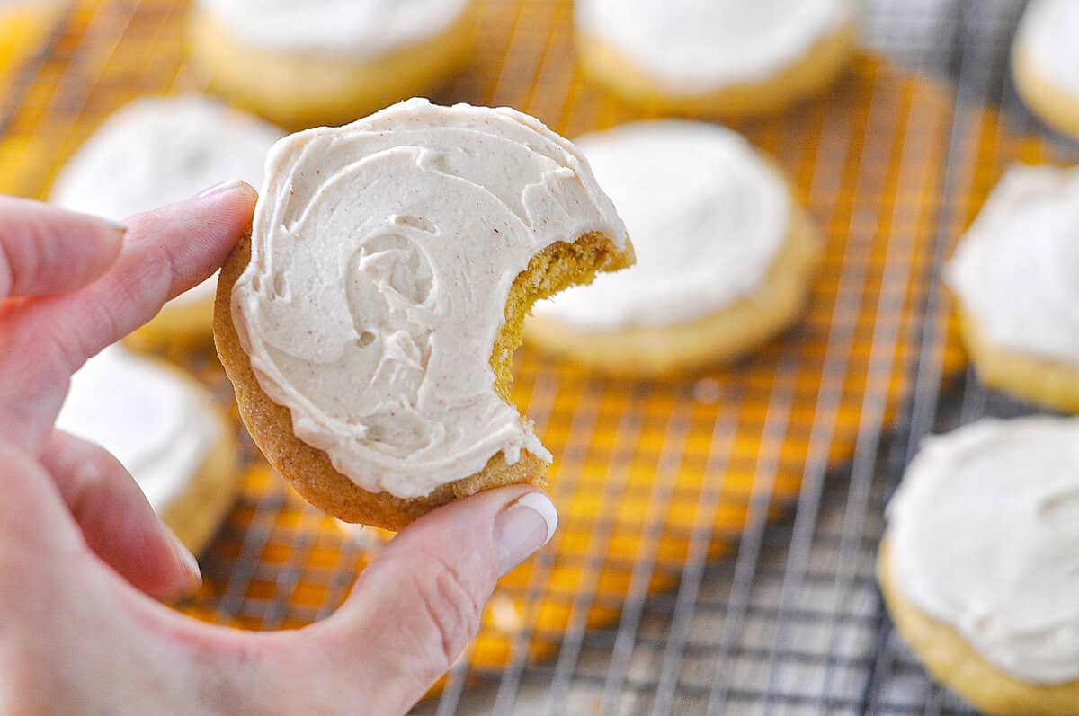 hand holding a frosted pumpkin sugar cookie with a bite missing from it