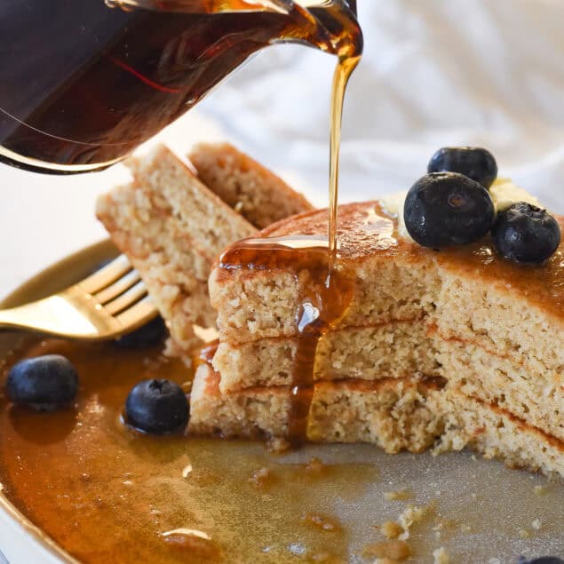 pouring syrup over whole wheat pancakes
