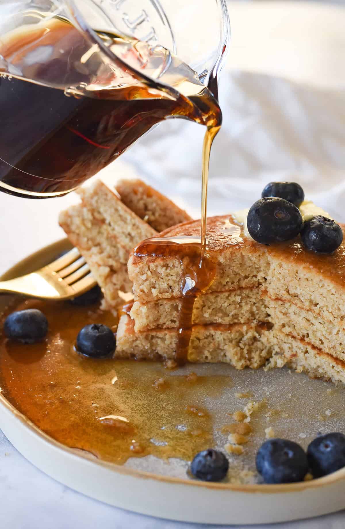 pouring syrup over whole wheat pancakes