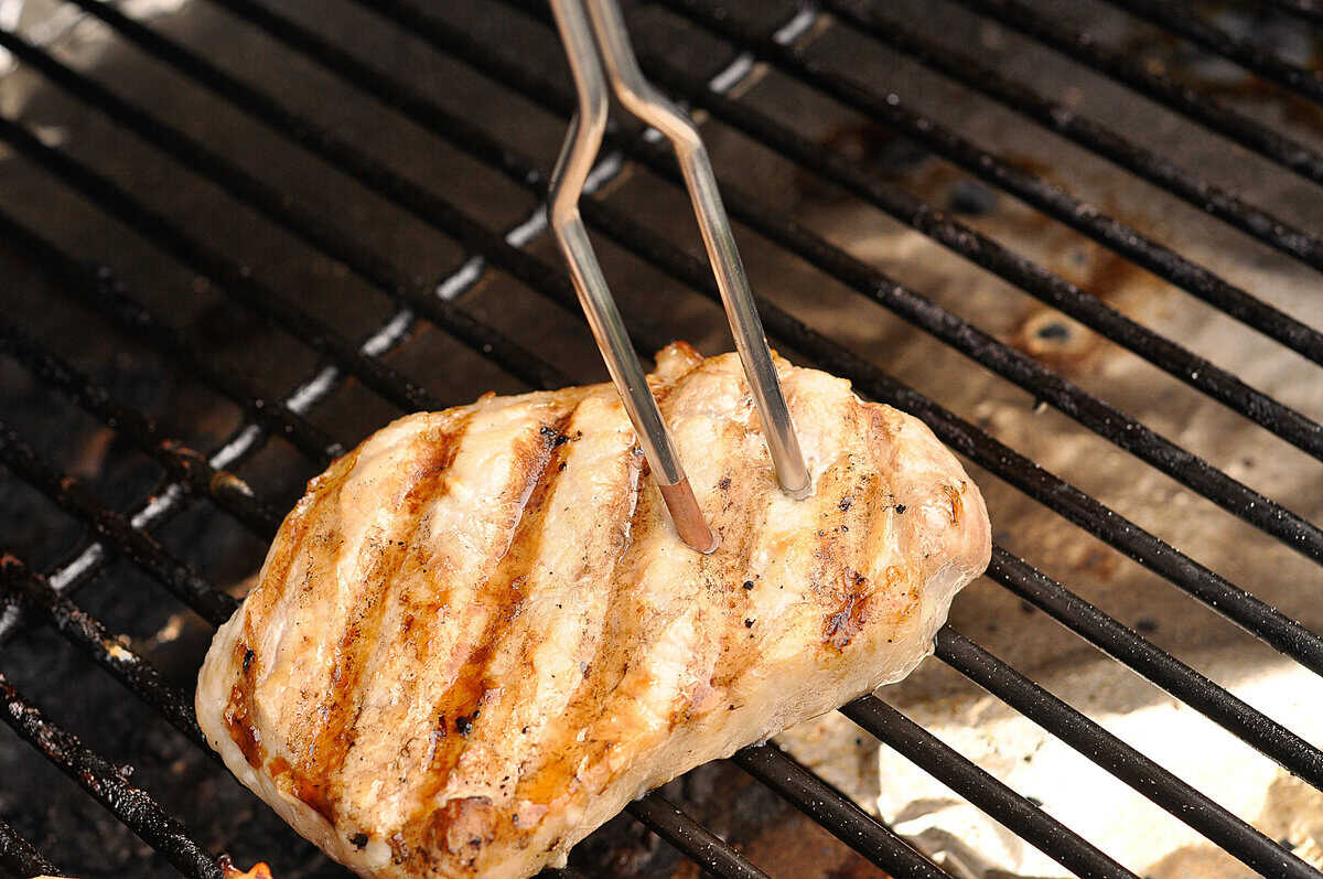 Grilled Pork Chop fork thermometer checking temperature of a brined pork chop on grill