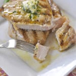 two pork chops on a plate with herb butter on top
