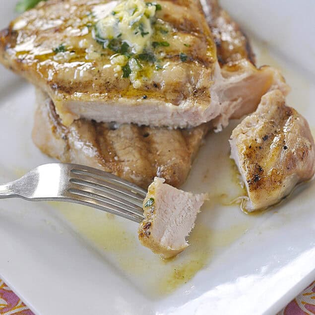 two pork chops on a plate with herb butter on top